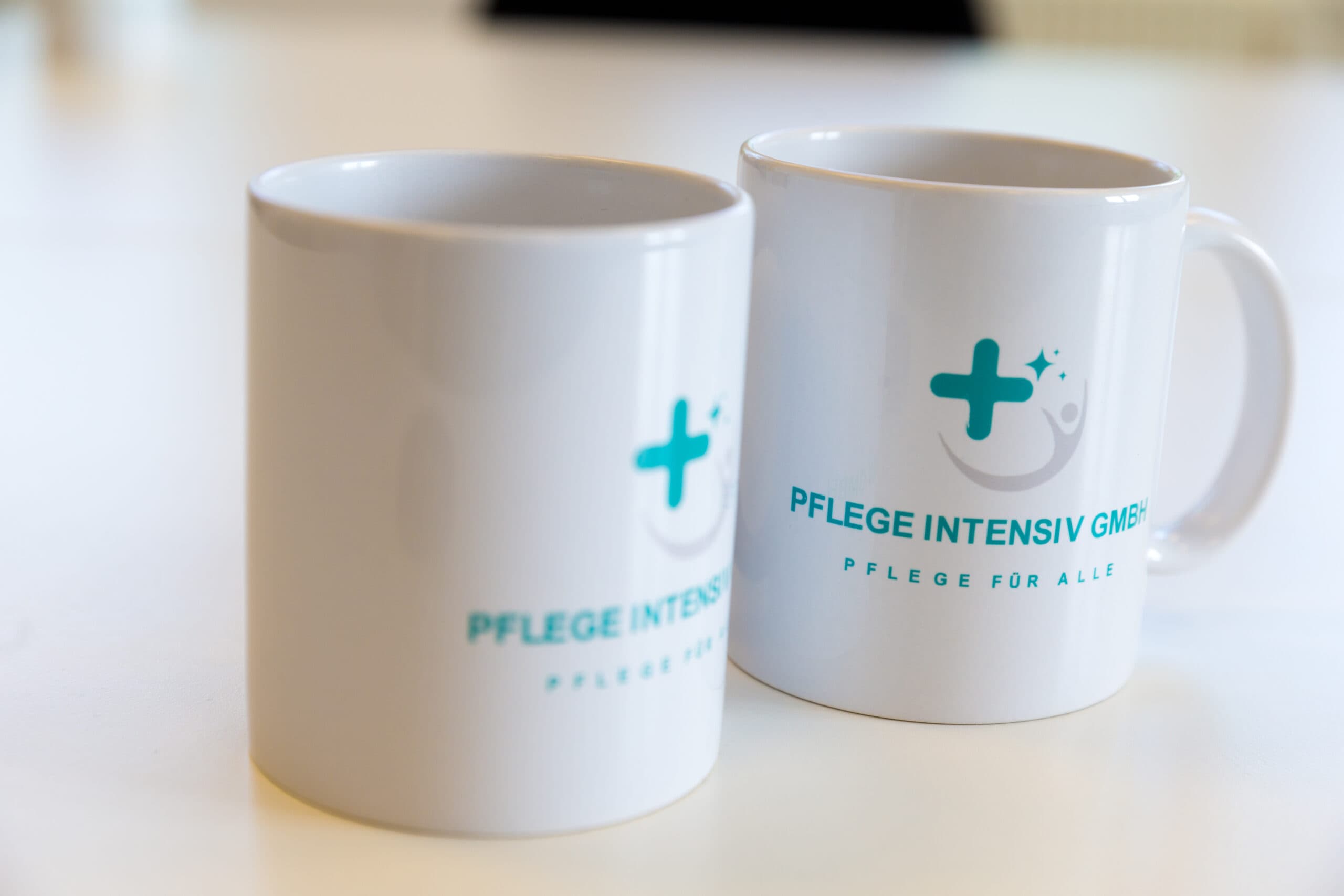Zwei Tassen mit dem Logo der Pflege Intensiv GmbH