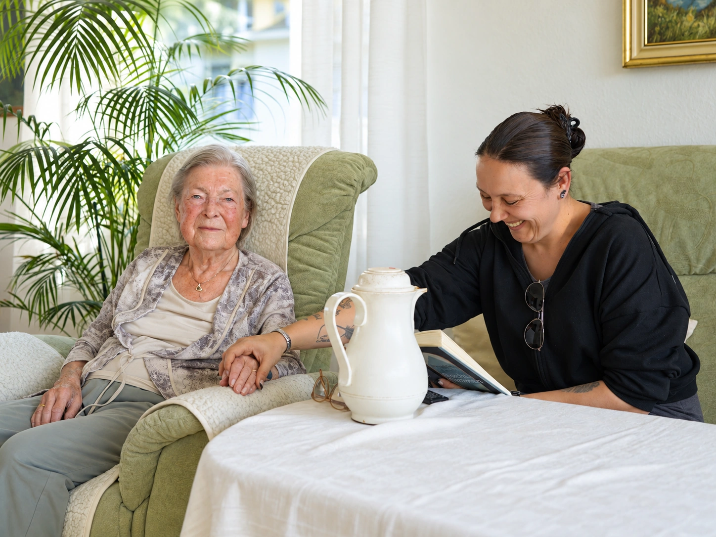 Alltagsbegleiterin sitzt bei einer Seniorin im Sessel, auf dem Tisch eine Kaffeekanne