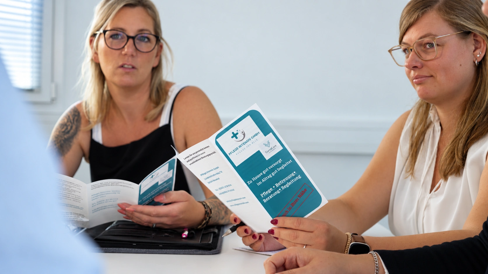 Beratungsgespräch am Tisch: Eine Mitarbeiterin zeigt einen Flyer zu den Leistungen der Pflegeversicherung