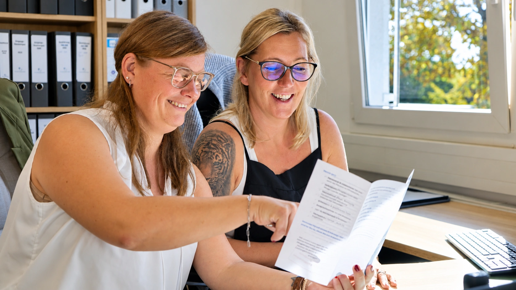 Zwei Mitarbeiterinnen gehen am Schreibtisch gemeinsam ein Schriftstück durch