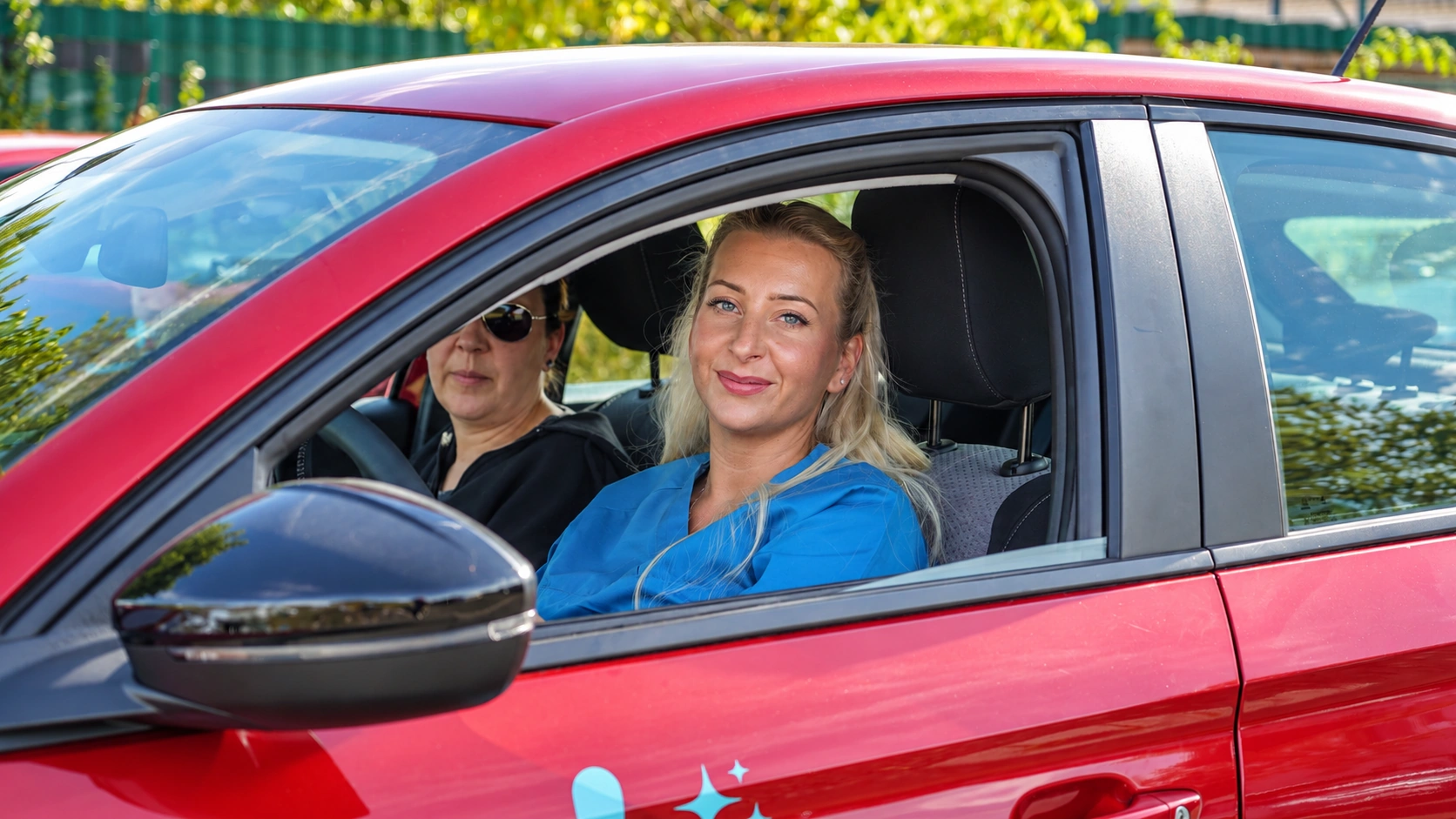 Zwei Mitarbeiterinnen der Pflege Intensiv GmbH im roten Dienstwagen auf dem Weg zum Einsatz