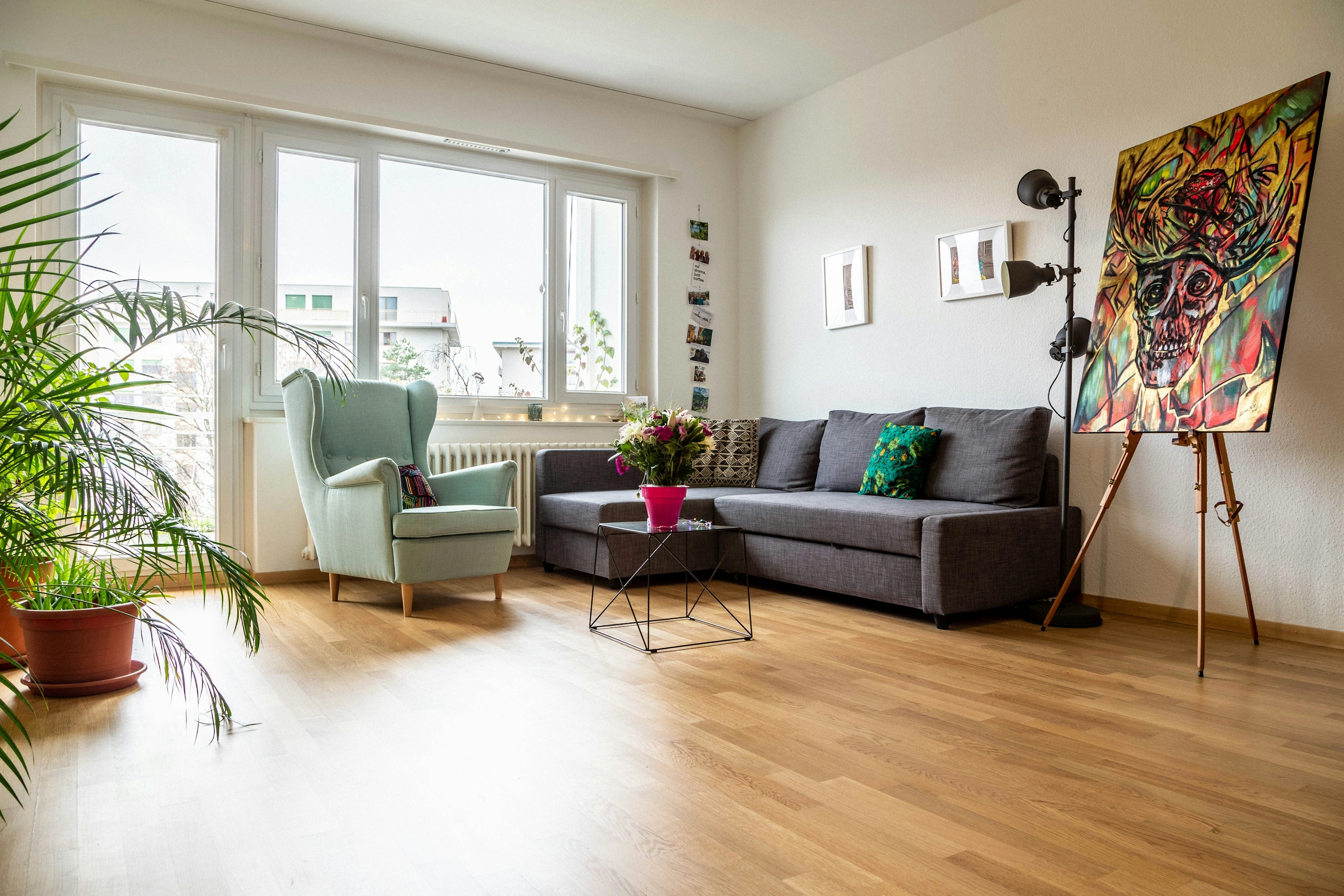 Helles, aufgeräumtes Wohnzimmer mit Sofa, Sessel und Pflanzen am Fenster